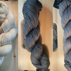 May include: Three skeins of yarn in different colors: white, gray, and a darker gray. The yarn is arranged in a spiral shape and is ready for knitting or crocheting.