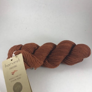 May include: A skein of brown fingering weight yarn labeled "harvest" with a tag that reads "Naturally hand dyed extrafine merino" and "urth" with the website address www.urthyarns.com and "Made in Iceland".