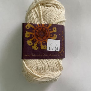 May include: A ball of natural, undyed organic cotton yarn in a cream color. The yarn is wrapped in a brown paper label with a colorful logo and the text "100% Naturally Dyed Organic Cotton" and "$7.00".