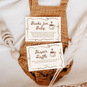 May include: Two baby shower cards with text: "Books for Baby" and "Diaper Raffle." The cards have a striped background and a coffee cup illustration. The cards are on a brown onesie.