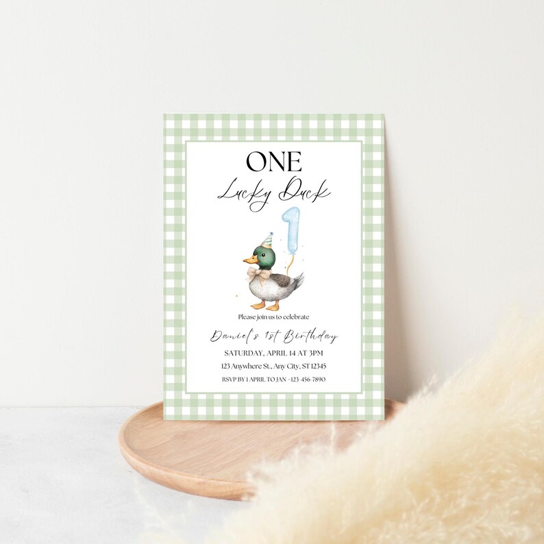 May include: A green and white gingham patterned invitation card with a cartoon duck wearing a party hat and holding a blue number one balloon. The text on the card reads "One Lucky Duck" and includes details for a first birthday party.