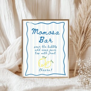 K&ouml;nnte beinhalten: Ein gerahmtes Schild mit den Worten "Mimosa Bar" in blauer Schrift. Das Schild hat einen blau-wei&szlig; gestreiften Hintergrund und enth&auml;lt Anweisungen und eine Zeichnung von zwei Zitronen. Die Worte "Cheers!" stehen unten.