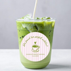 May include: A refreshing matcha latte in a clear plastic cup with ice. A pink and white striped sticker on the cup reads "She found her perfect matcha!" with a teacup graphic and bridal shower details.