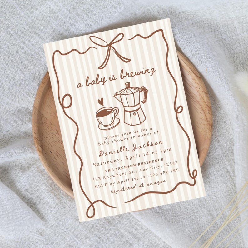 May include: A baby shower invitation with a coffee theme. The invitation features a brown and white striped background with a decorative border. The text "a baby is brewing" is at the top, along with a coffee cup and a moka pot illustration.