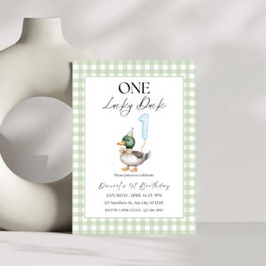 May include: Green and white gingham patterned invitation with a cartoon duck wearing a party hat and holding a blue number one balloon. The text reads "ONE Lucky Duck" and "Daniel's 1st Birthday".
