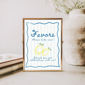 K&ouml;nnte beinhalten: Ein gerahmtes Schild mit goldenem Rand zeigt das Wort "Favors" in blauer Schrift, den Text "Please take one!" und gelbe Zitronenillustrationen. Das Schild enth&auml;lt auch den Text "Thank you for celebrating with us!" auf gestreiftem Hintergrund.