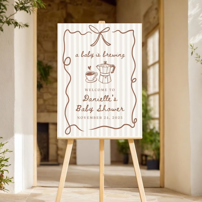 May include: A white and brown striped sign with a brown ribbon and the text "a baby is brewing" and a coffee pot and cup illustration. The sign also says "Welcome to Danielle's Baby Shower" and "November 24, 2025".