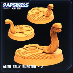 Op de afbeelding: Drie oranje Alien Belly Burster - A beeldjes. Elke figuur toont een gedetailleerd buitenaards wezen dat oprijst uit een cirkelvormige basis met een toetsenbordachtig ontwerp. De linkerbovenhoek heeft de tekst "Papsikels May 2021".
