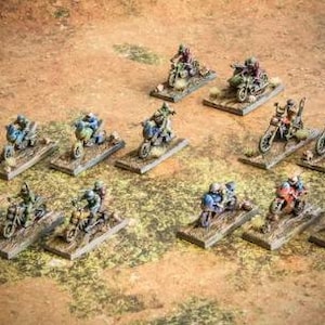 Könnte beinhalten: Miniaturfiguren von Motorradfahrern auf Sockeln, bemalt in verschiedenen Farben. Die Motorräder sind detailliert mit realistischen Merkmalen, und die Fahrer tragen Helme und Ausrüstung. Die Szene spielt auf einer strukturierten, braunen Oberfläche.