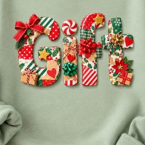 以下が含まれることがあります： セージグリーンのスウェットシャツに「GIFT」という文字が大きくプリントされています。各文字は、クリスマスの模様、赤いリボン、小さなギフトボックス、ペパーミントキャンディ、金色の星、赤と緑のヒイラギの葉で装飾されています。