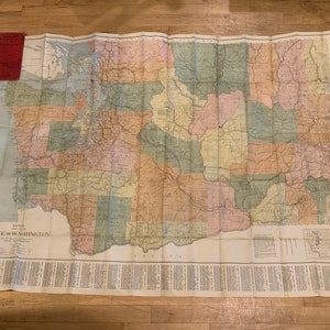 May include: A vintage map of the state of Washington, showing the counties and major roads. The map is printed on a cream-colored paper and has a red title bar at the top.
