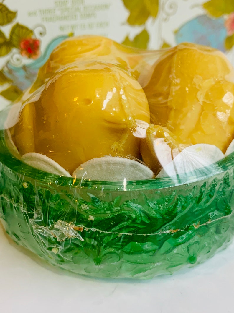 Puede incluir: Dos jabones amarillos con forma de p&aacute;jaro en un nido de pl&aacute;stico verde con un dise&ntilde;o floral blanco. Los jabones est&aacute;n envueltos en pl&aacute;stico transparente.