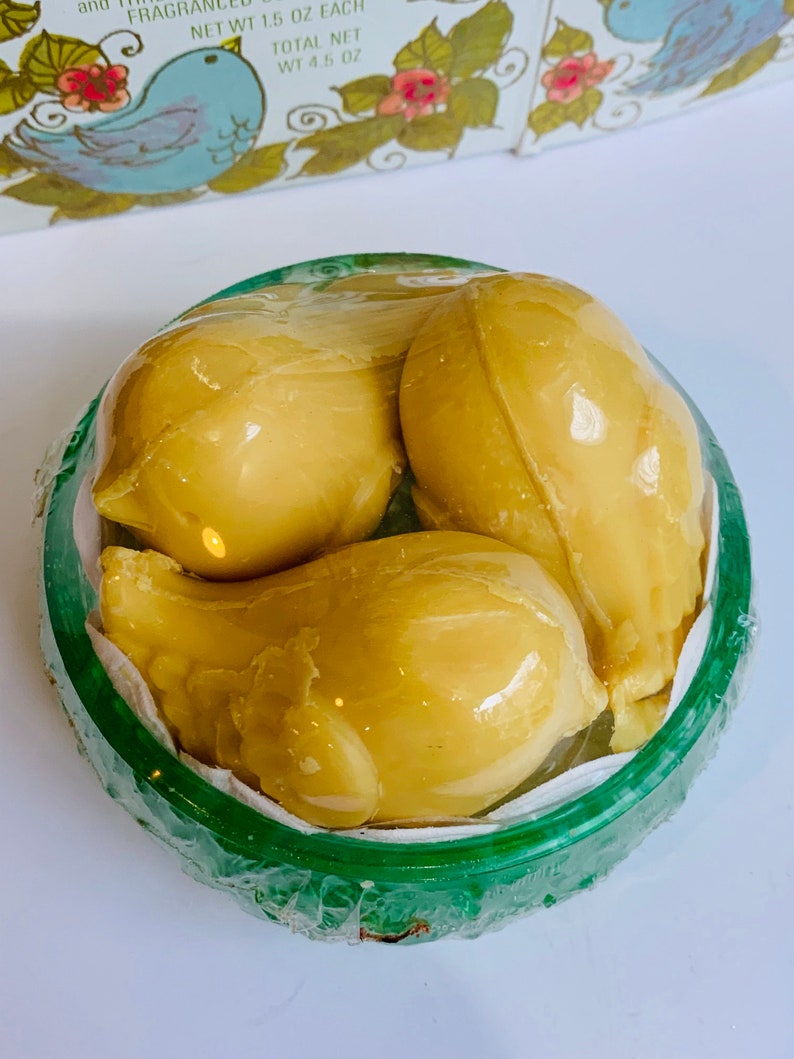 Puede incluir: Tres jabones amarillos con forma de p&aacute;jaro en un recipiente verde. Los jabones est&aacute;n dispuestos en forma de nido.