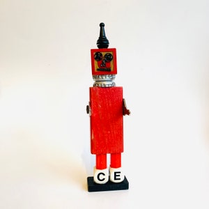 May include: A red wooden robot with a black top hat, black eyes, and white and silver details. The robot is standing on a black base with white letters that spell "CE".