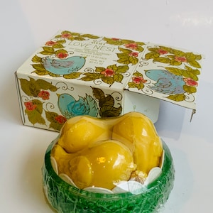 Puede incluir: Un juego de tres jabones amarillos con forma de p&aacute;jaro en un recipiente verde con forma de nido. La caja es blanca con un dise&ntilde;o floral y el texto "Avon Love Nest Soap Dish Three Fragranced Soaps Net Wt 1.5 oz Each Total Net Wt 4.5 oz".