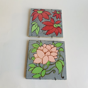 May include: Two square ceramic tiles with floral designs. The top tile features red and green flowers on a gray background. The bottom tile features pink and green flowers on a gray background.