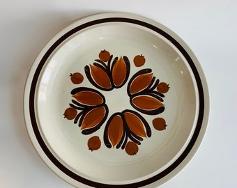 May include: A white ceramic dinner plate with a brown and orange floral design. The plate has a brown rim.