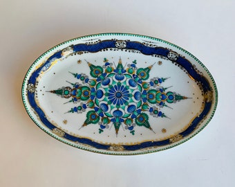 May include: An oval ceramic serving dish with a blue and green mandala design. The mandala is surrounded by a gold and blue border.