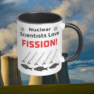 May include: White ceramic mug with a black rim and handle. The mug has a black and white illustration of fishing rods and fish. The text on the mug reads "Nuclear Scientists Love FISSION!"