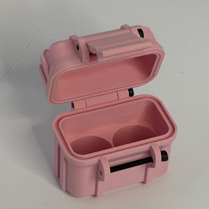 May include: A pink, rectangular, open case with a hinged lid. The case has a rubber seal and two circular compartments inside. The case has a black handle and black latches. The case is made of a hard plastic material.