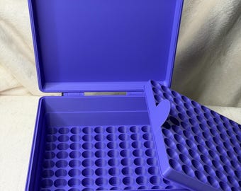 May include: A purple storage case with an open lid, revealing a grid of circular compartments. The case has a handle and latches for secure closure. The lid also has a grid of circular compartments. The case is designed for organizing small items.