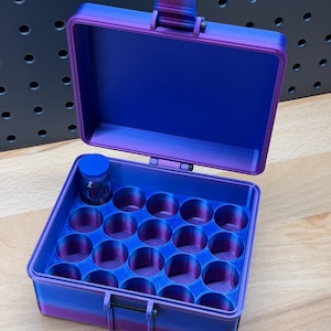 May include: A blue and purple gradient storage case with an open lid. The interior has multiple circular compartments, and a small glass bottle sits inside. The case is made of plastic and has a latch closure.