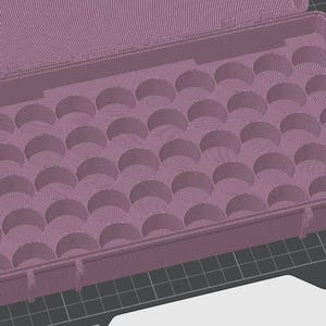 May include: A mauve-colored, open rectangular case with a hinged lid. The interior is designed with numerous semi-circular indentations, likely for holding small, round objects. The case has a textured surface and is designed with a latch.