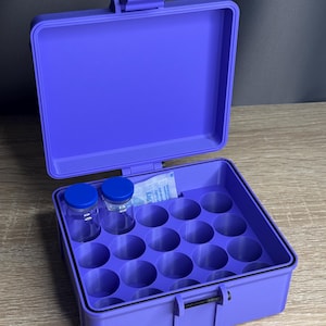 May include: A purple storage case with an open lid, revealing a grid of circular compartments. Two small glass bottles with blue caps are visible. A packet is also inside the case. The case is designed to hold small items.