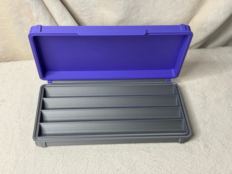 May include: An open, two-tone storage case with a purple lid and a gray base. The interior of the base features multiple gray compartments. The case is designed to hold and organize small items.