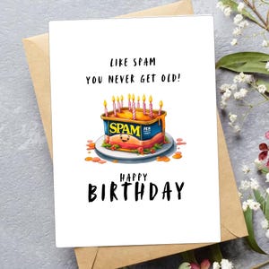 Op de afbeelding: Een verjaardagskaart met een humoristische illustratie van een blik Spam met kaarsen erop. De tekst luidt "Net als Spam word je nooit oud!" en "Happy Birthday".