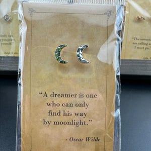 May include: Silver crescent moon earrings with textured detailing, displayed on a card with a quote by Oscar Wilde: "A dreamer is one who can only find his way by moonlight."
