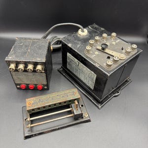 May include: Three vintage electrical components: a small black box with multiple connectors, a larger black box with dials and labels, and a small metal device with the text "NO81".
