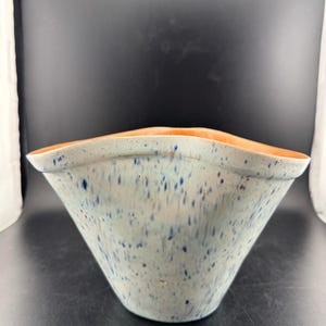 Pode incluir: Uma tigela de cerâmica com uma forma assimétrica única. O exterior é azul claro com salpicos azuis escuros, enquanto o interior tem um tom laranja quente. A borda tem um design ondulado. Esta tigela decorativa é adequada para vários usos.