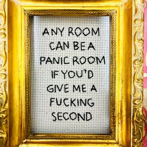 May include: A framed cross-stitch piece with the text "ANY ROOM CAN BE A PANIC ROOM IF YOU'D GIVE ME A FUCKING SECOND." The frame is ornate, gold-colored, and rectangular, with a white cross-stitch background.
