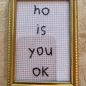 May include: A framed cross-stitch with the text "ho is you ok" in black thread on a white background.