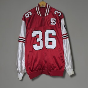 May include: A red and white varsity jacket featuring the number 36 in large white numerals on the front, the number 6 on the right shoulder, the number 3 on the left shoulder, and the letters NC stacked vertically on the upper left chest area.