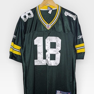 Puede incluir: Camiseta de fútbol verde y amarilla con el número 18 en blanco. La camiseta tiene rayas blancas y amarillas en las mangas y el cuello. El logotipo de la NFL es visible en el cuello.