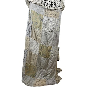 May include: A long skirt featuring a patchwork design of various light-colored fabrics with floral and botanical patterns in shades of beige, cream, and soft gray. The garment is topped with a cream-colored crocheted fabric at the waistline.