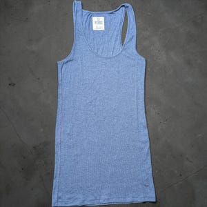 Peut inclure: Un débardeur dos nageur bleu clair chiné avec une encolure dégagée. Le vêtement présente une étiquette de col intérieure blanche avec le texte PINK imprimé en noir. Le tissu a un aspect texturé subtil et un ourlet droit au bas du vêtement.