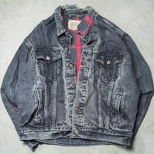 May include: A black acid-wash denim jacket featuring a red and black plaid flannel lining, a pointed collar, metal button closures, two chest pockets with buttoned flaps, and two side slit pockets. The jacket has a distressed, worn-in appearance.
