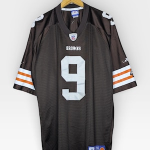 Pode incluir: Camisola de futebol castanha com o número 9 em branco. A camisola tem riscas brancas e laranja nas mangas e a palavra "BROWNS" acima do número. A camisola está pendurada num cabide de madeira.