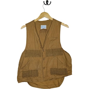 May include: A tan-colored vest with multiple pockets and a button-up front. The vest is hanging on a wooden hanger. The vest has a label on the upper chest area. The vest is made of a lightweight material.
