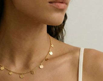 Può includere: Una delicata collana dorata con piccoli ciondoli a disco rotondi. La collana è indossata intorno al collo, con i ciondoli distanziati lungo la catena. Il gioiello è un accessorio semplice ma elegante.