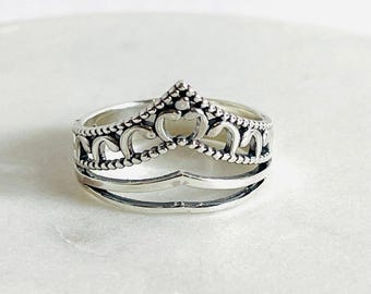 Könnte beinhalten: Ein silberner Ring mit einem zarten Kronendesign. Der Ring besteht aus zwei Bändern, eines mit einem detaillierten Kronendesign und das andere ein einfaches Band.