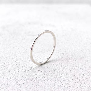 Könnte beinhalten: Ein dünner, polierter silberfarbener Metallring mit einem glatten, abgerundeten Band. Der Ring zeichnet sich durch ein schlichtes, kreisförmiges Design mit einer reflektierenden Oberfläche aus, die das Licht einfängt und gleichmäßig wirkt.