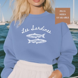 May include: A light blue sweatshirt with the text "Les Sardines" and a white illustration of two sardines.