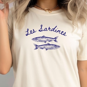 May include: A white t-shirt with a blue graphic of two sardines and the text "Les Sardines".
