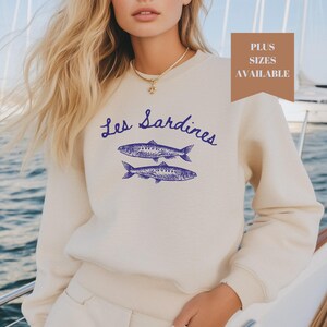 May include: A cream colored sweatshirt with a blue graphic of two sardines and the text "Les Sardines" on the front.
