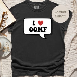 May include: Black t-shirt with a white speech bubble that says "I ♥ OOMF". The speech bubble has a red heart in it. The shirt is from Comfort Colors.