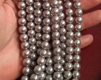 May include: A strand of silver-colored pearl beads. The beads are round and smooth, and they are strung together on a clear thread.